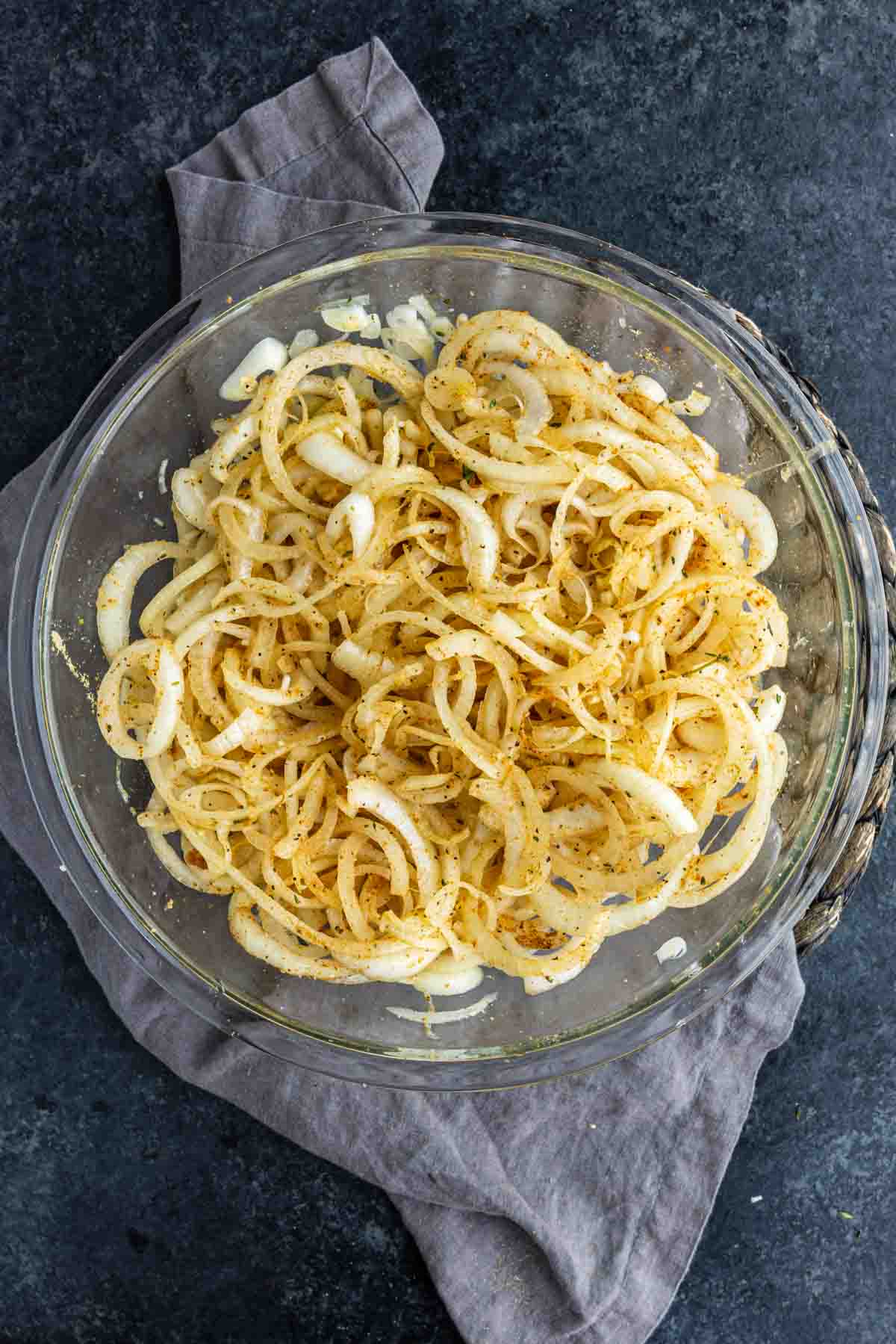 Sliced Tennessee onions tossed with seasoning in a glass bowl.