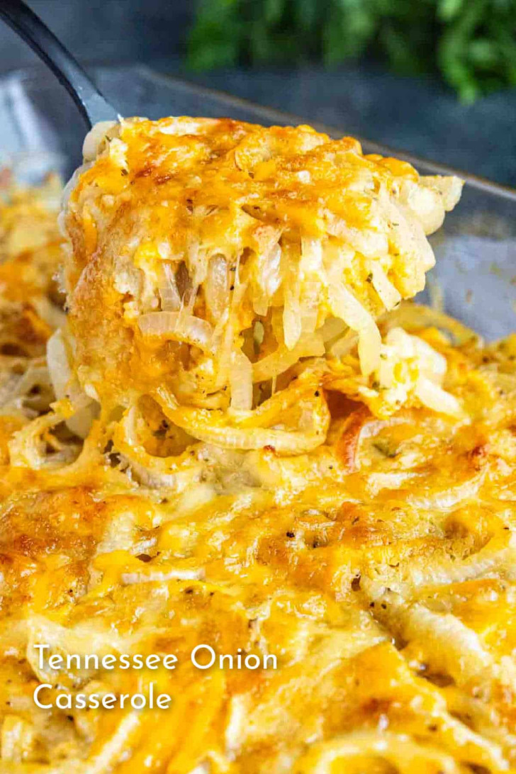 A spatula lifts a portion of cheesy Tennessee Onion Casserole from a glass baking dish.